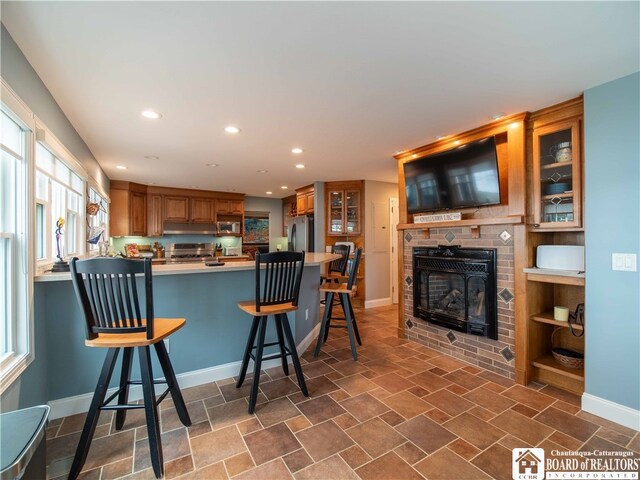 kitchen featuring a breakfast bar, glass insert cabinets, brown cabinets, and stainless steel appliances