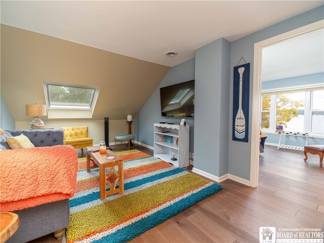 playroom with lofted ceiling with skylight, visible vents, baseboards, and wood finished floors