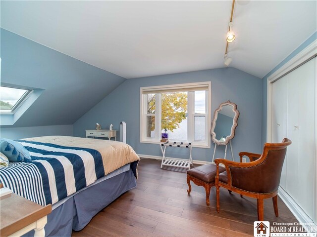 bedroom with lofted ceiling with skylight, rail lighting, wood finished floors, and baseboards