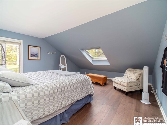 bedroom featuring baseboards, lofted ceiling with skylight, and wood finished floors