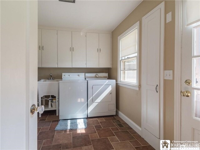 laundry room with washer and dryer, stone finish floor, cabinet space, and baseboards