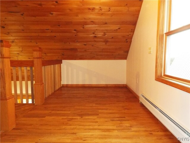 additional living space with vaulted ceiling, a baseboard heating unit, and light hardwood / wood-style flooring