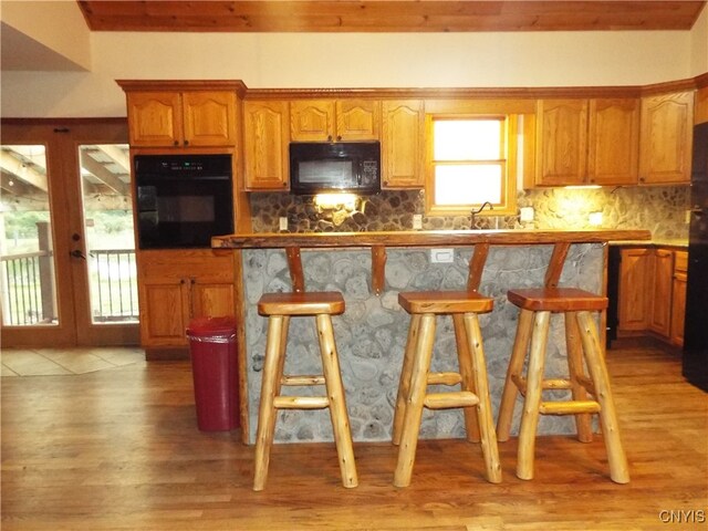 kitchen featuring light wood-type flooring, black appliances, a kitchen bar, and backsplash