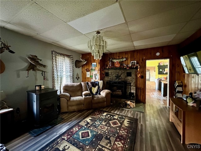 living room featuring wooden walls, hardwood / wood-style flooring, a drop ceiling, an inviting chandelier, and a fireplace