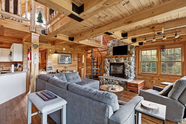 living room with wood-type flooring, a stone fireplace, beamed ceiling, and wood walls