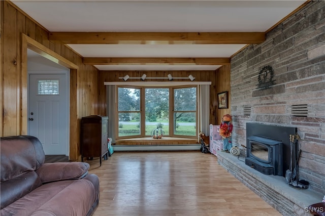 living room featuring light hardwood / wood-style floors, wooden walls, beam ceiling, and a wood stove