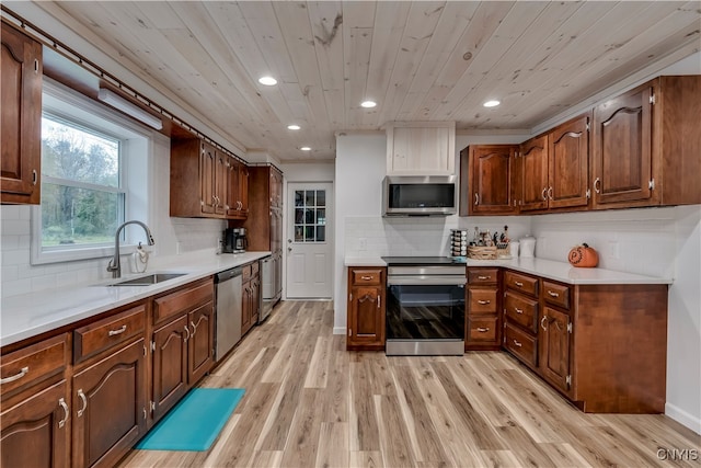 kitchen with appliances with stainless steel finishes, backsplash, light wood-type flooring, and sink