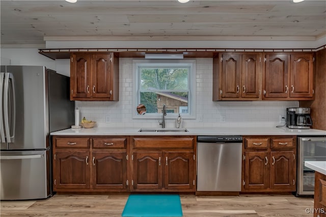 kitchen featuring appliances with stainless steel finishes, tasteful backsplash, light wood-type flooring, beverage cooler, and sink