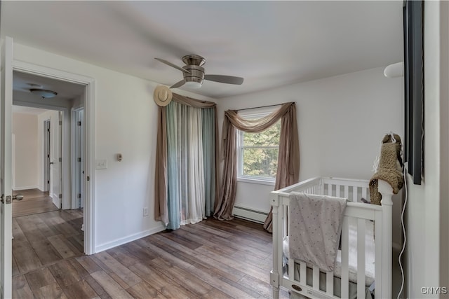 bedroom with ceiling fan, a nursery area, hardwood / wood-style flooring, and a baseboard radiator