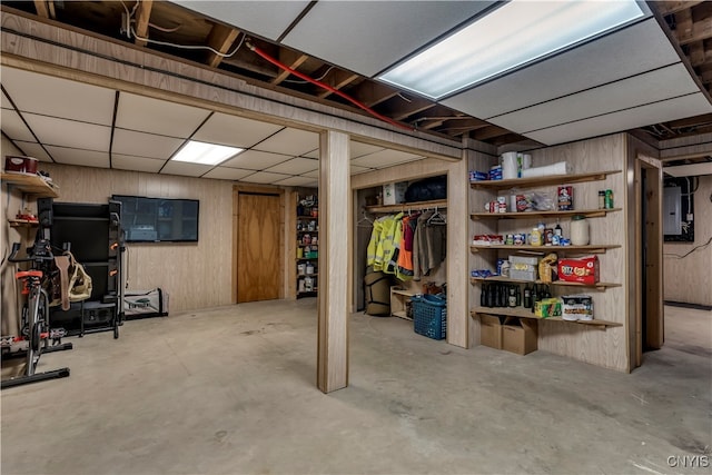 basement with electric panel, wooden walls, and a drop ceiling