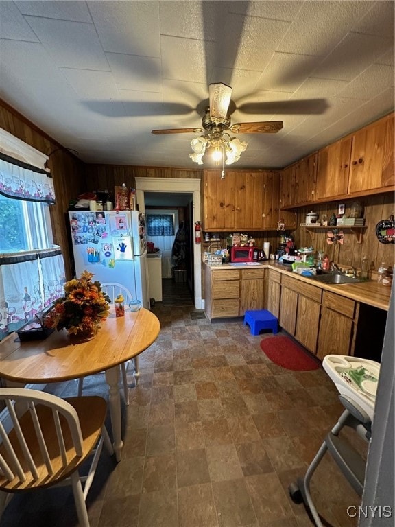 kitchen with wood walls, ceiling fan, sink, and white refrigerator