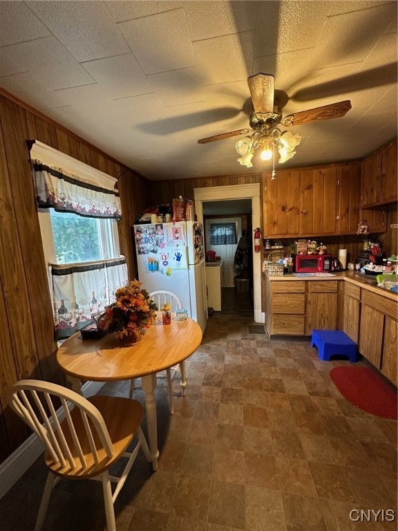 kitchen with wood walls, ceiling fan, and white fridge