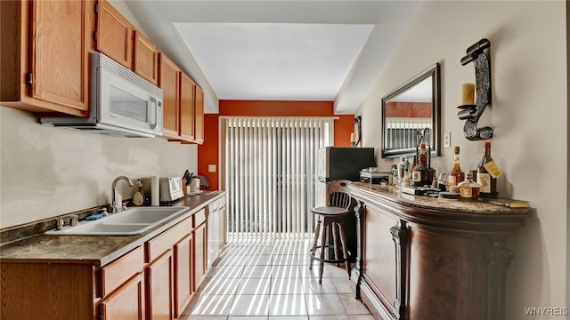 kitchen with white appliances, a kitchen bar, sink, and light tile patterned floors