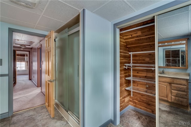 interior space featuring a drop ceiling, wooden walls, walk in shower, and vanity