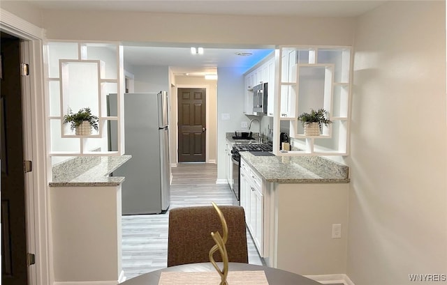 kitchen with light stone countertops, light hardwood / wood-style floors, appliances with stainless steel finishes, and white cabinetry