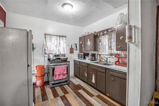 kitchen with appliances with stainless steel finishes, hardwood / wood-style floors, dark brown cabinets, and sink