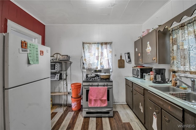 kitchen with appliances with stainless steel finishes, ornamental molding, hardwood / wood-style floors, and sink