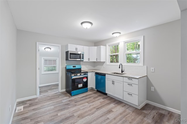 kitchen with light stone counters, sink, white cabinetry, light hardwood / wood-style flooring, and appliances with stainless steel finishes