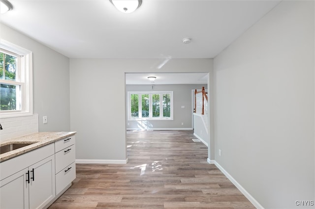 kitchen featuring light wood-type flooring, light stone countertops, white cabinetry, and sink