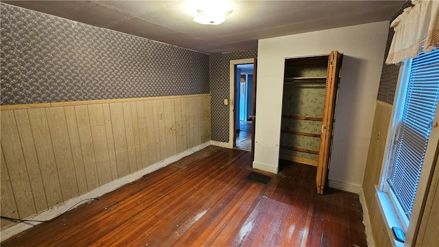 unfurnished bedroom with wood walls, a closet, and dark hardwood / wood-style flooring