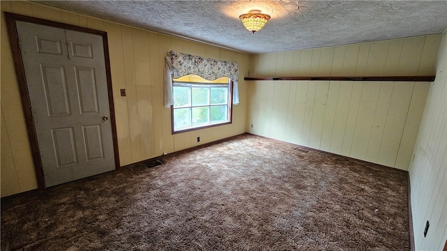 unfurnished room with wood walls, a textured ceiling, and carpet floors