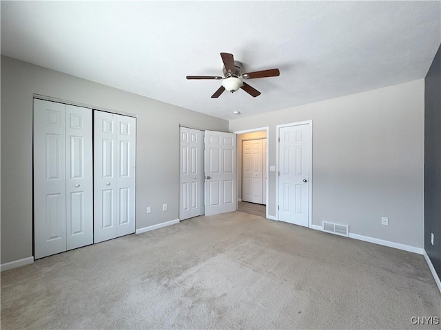 unfurnished bedroom featuring two closets, ceiling fan, and light colored carpet