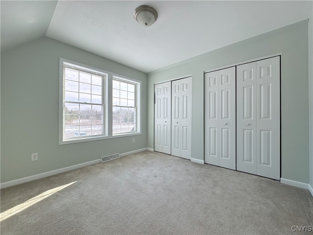 unfurnished bedroom featuring light carpet, vaulted ceiling, and multiple closets