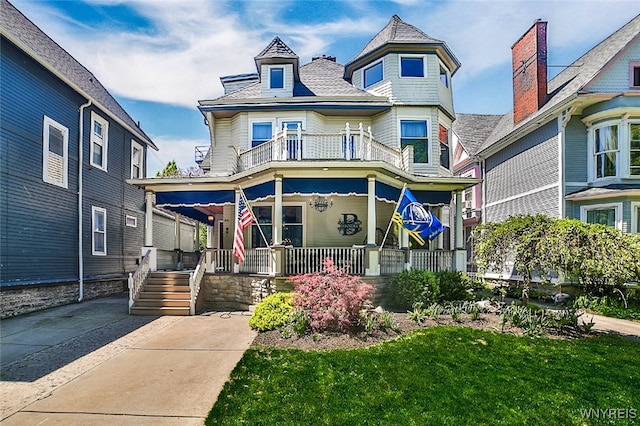 victorian-style house with a balcony, a porch, and a front lawn