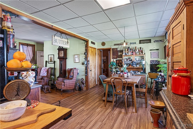 dining space with wood-type flooring, bar, and a paneled ceiling