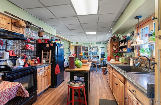 kitchen with light wood-type flooring, black appliances, sink, and a paneled ceiling