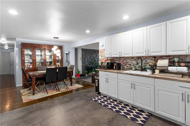 kitchen with hanging light fixtures, decorative backsplash, white cabinetry, dark wood-type flooring, and sink