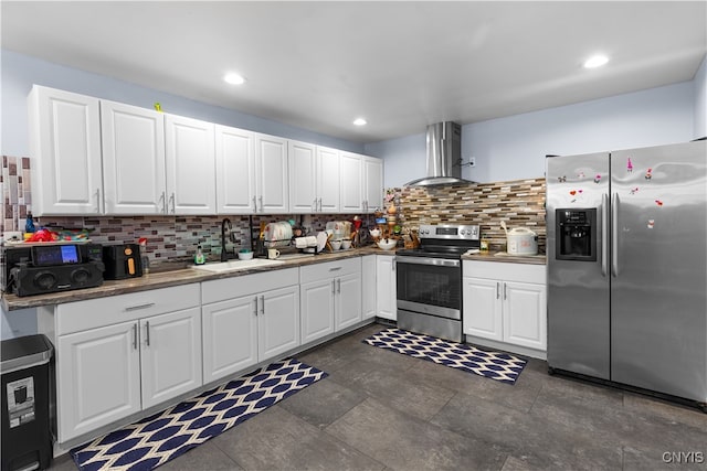 kitchen with appliances with stainless steel finishes, white cabinetry, tasteful backsplash, sink, and wall chimney range hood