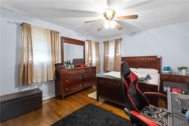 bedroom featuring a baseboard heating unit, ceiling fan, multiple windows, and dark wood-type flooring