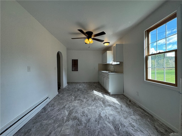 interior space with ceiling fan, sink, backsplash, a baseboard heating unit, and white cabinetry