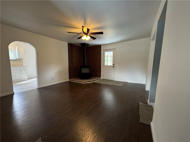 unfurnished living room featuring ceiling fan, dark hardwood / wood-style floors, and a wood stove