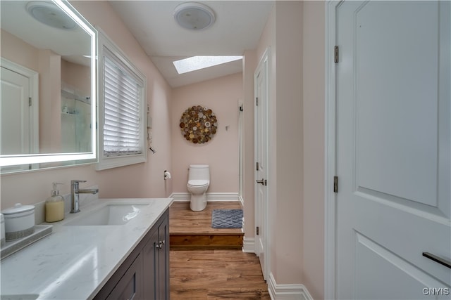 bathroom with vaulted ceiling with skylight, walk in shower, toilet, hardwood / wood-style floors, and vanity