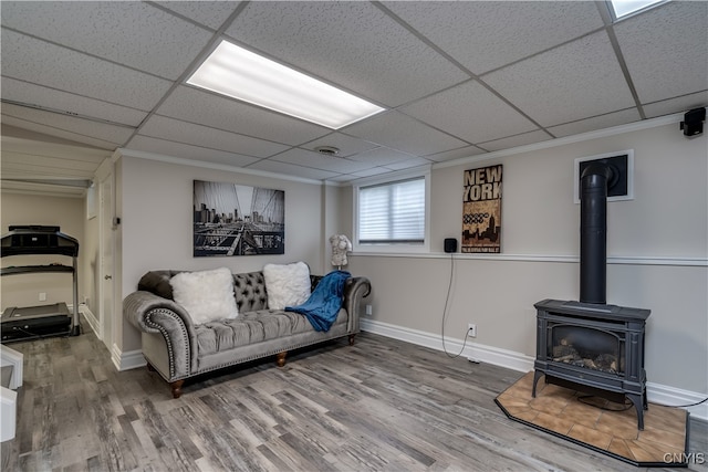 living room featuring hardwood / wood-style flooring, crown molding, a wood stove, and a paneled ceiling