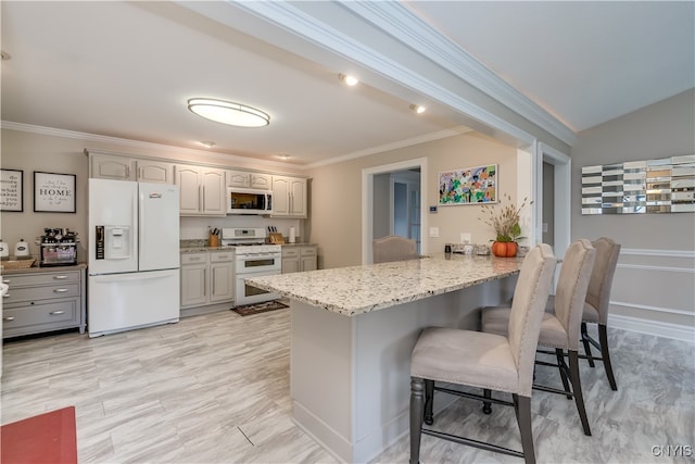 kitchen featuring white appliances, a kitchen breakfast bar, light stone countertops, ornamental molding, and kitchen peninsula