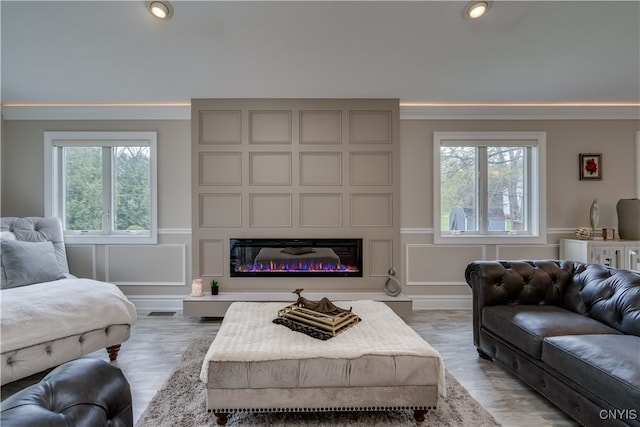 living room featuring a fireplace, light wood-type flooring, ornamental molding, and a wealth of natural light