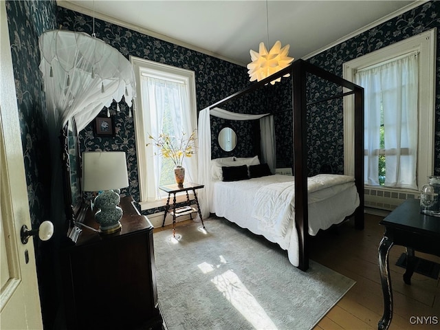 bedroom featuring wood-type flooring, radiator heating unit, crown molding, and multiple windows