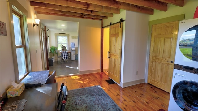 washroom featuring a barn door, stacked washer and clothes dryer, and hardwood / wood-style flooring