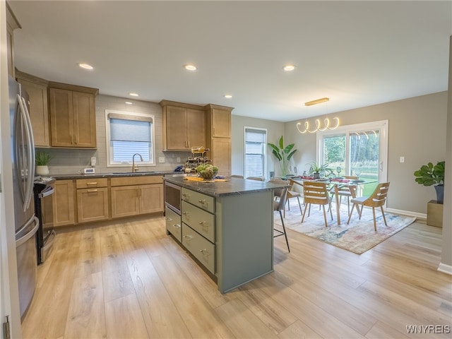 kitchen featuring light wood-type flooring, a center island, sink, pendant lighting, and backsplash