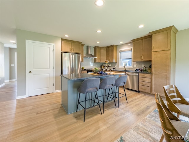 kitchen with backsplash, wall chimney range hood, stainless steel appliances, a center island, and light hardwood / wood-style floors