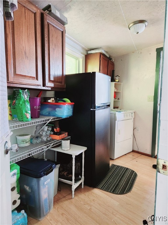 kitchen featuring washer / clothes dryer, stainless steel refrigerator, and light wood-type flooring