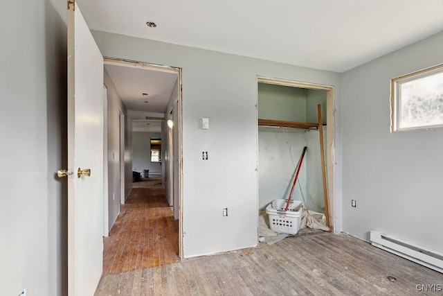 unfurnished bedroom featuring a baseboard radiator, a closet, and wood-type flooring