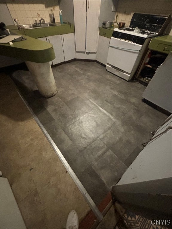 interior space with white cabinets, white gas range, and decorative backsplash