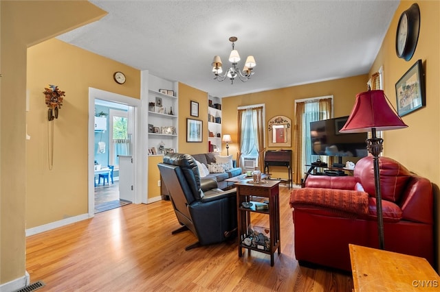 living room featuring a notable chandelier, light hardwood / wood-style flooring, built in features, and a textured ceiling