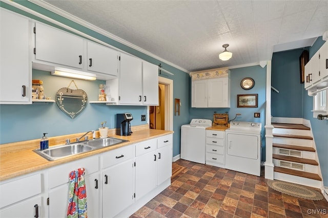 kitchen with crown molding, white cabinetry, washer and clothes dryer, and sink