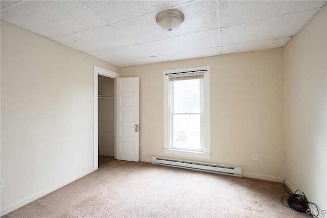 carpeted spare room with baseboard heating, a drop ceiling, and a wealth of natural light