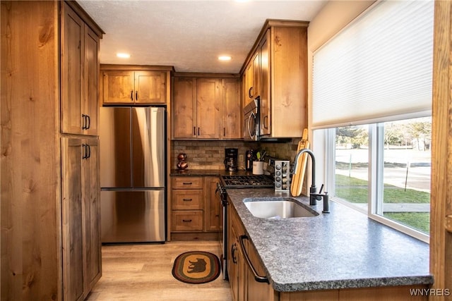 kitchen with sink, stainless steel appliances, dark stone countertops, decorative backsplash, and light wood-type flooring